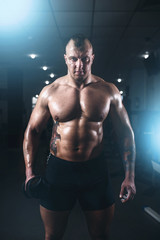 Fototapeta na wymiar Muscular athlete posing with dumbbell in sport gym