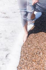 the girl's leg on the sea in a blue dress goes stepping stones sand summer water nature river waves