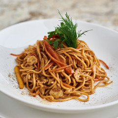 Flat egg noodles with vegetables served in big white ceramic round plate with glass of white wine on marble table