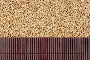 Beautiful bamboo mat on barley grains as agricultural background.