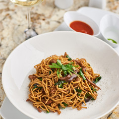 Flat egg noodles with duck meat, chicken, shiitake mushrooms served on white plate with white garlic and red spicy sauce