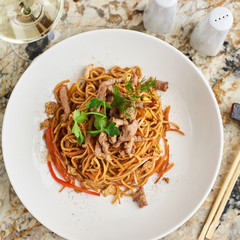Flat egg noodles with pork slices served on white plate with white garlic and red spicy sauce