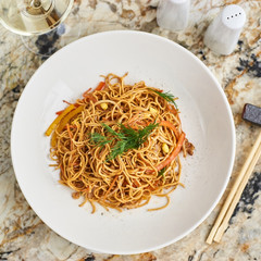 Flat egg noodles with pork slices served on white plate with white garlic and red spicy sauce