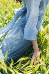 girl in a gray blue dress goes on green field, hands touching ears, close-up