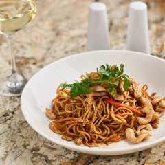 Thin egg noodles with chicken slices served on white plate with white garlic and red spicy sauce