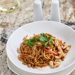 Thin egg noodles with chicken slices served on white plate with white garlic and red spicy sauce