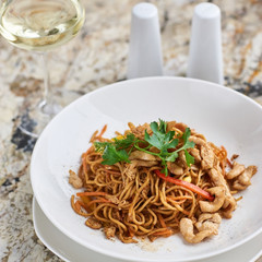 Thin egg noodles with chicken slices served on white plate with white garlic and red spicy sauce
