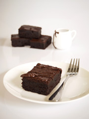 Sliced brownies on white plate. Served with chocolate fudge topping. On white plate over white background.