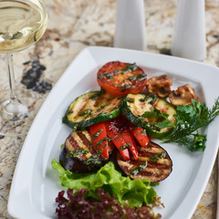Grilled vegetables served on white plate. Eggplant, tomato, paprika and Zucchini slices.