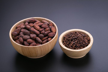 Chocolate bar and dried cocoa pod, cocoa nibs in wooden bowl on black background