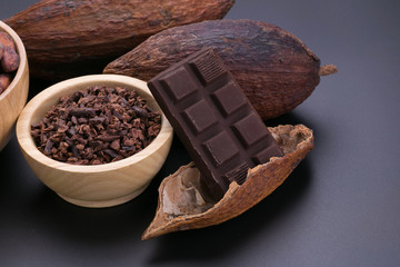 Chocolate bar and dried cocoa pod, cocoa nibs in wooden bowl on black background
