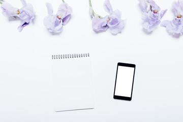 Mobile phone, notebook and blue flowers lie on a white background