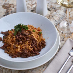 Fried rice with beef slices served in white round plate with glass of white wine on marble table