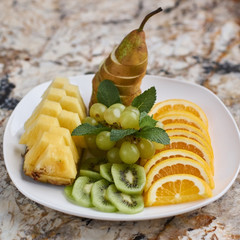 Fruit plate with pineapple, orange, kiwi, grape and pear on marble table.