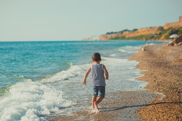 The boy running on a beautiful beach. The boy walking on a beautiful beach. Sea foam on the sand. lifestyle relationship contact pedigree ancestry