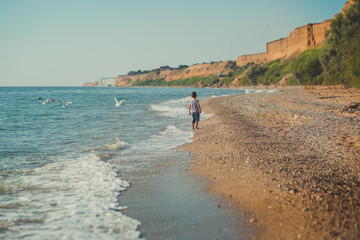 The boy running on a beautiful beach. The boy walking on a beautiful beach. Sea foam on the sand....