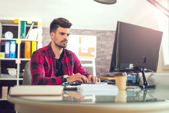 Handsome caucasian man at work desk facing flat screen computer screen in office