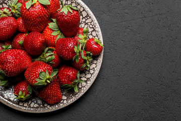 fresh ripe useful fruit strawberry in a clay bowl closeup on a black background