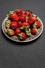 fresh ripe useful fruit strawberry in a clay bowl closeup on a black background