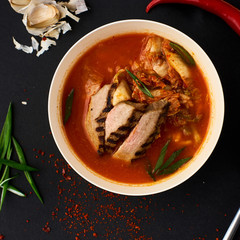 Korean cuisine. Spicy kimchi soup served in a bowl standing on black background.