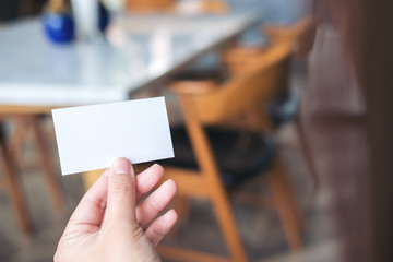 An image of a hand holding empty business card in modern cafe