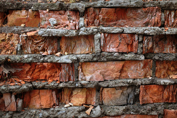 The texture of a ruined wall of red clay bricks and cement mortar.