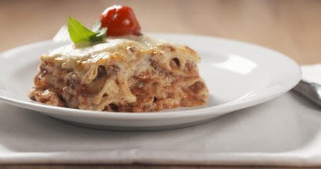 homemade lasagna portion on white plate on wood table