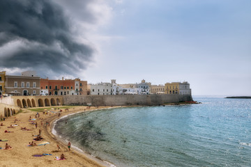 Fototapeta na wymiar Beach and old town of Gallipoli under clouds of brewing thunderstorm, selective focus, Puglia, Italy