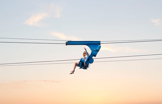 horizontal image of a young woman taking an air ride on a zip line in the early evening sun setting.