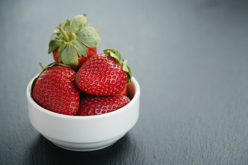 ripe organic strawberries in white bowl on slate background