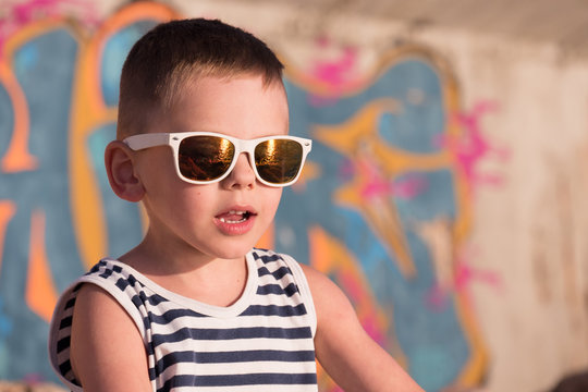 surprised little boy wearing sunglasses and sailor shirt on graffiti background