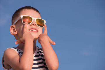 happy kid wearing sunglasses with sea sunset reflection on blue sky background