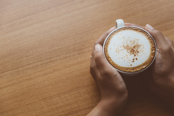 Top view of Hands holding a hot coffee in white cup on the wooden table.