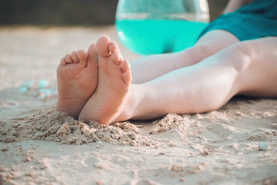 The girl's feet sitting on the beach.