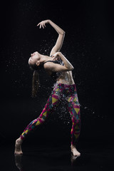 The girl dances on the floor covered with water on a black background