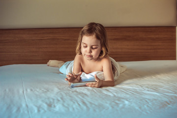 Happy little baby girl 4-5 years of European appearance holds a cell phone in her hand and checks the mail through the Internet. The concept of modern wireless technologies. © serperm73