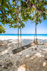 Wooden Swing and weathered rope on Beautiful tropical beach, white sand and blue sky background.