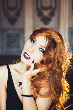 close-up portrait of young beautiful red-haired girl in the image of a Gothic witch on Halloween on a background of wax candles, fire, magic crystals and stones in the black dress conjures