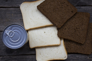 Closed canned food near sliced bread on wooden background