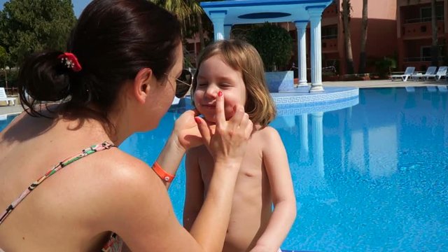 A beautiful European woman puts sunscreen on a child. A girl and a mother of European appearance. The kid is 4-5 years old. The concept of luxury rest on a luxury expensive resort.