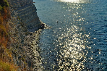 Obraz premium the sun reflected in the waves of the sea, steep cliff and rocks