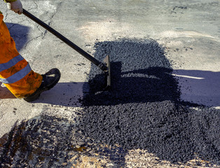 worker leveling fresh asphalt during asphalt pavement repair or construction works