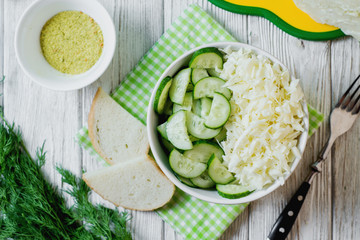  vegetarian Healthy food, light, low calorie fitness salad of fresh cucumbers, cabbage and dill with olive or sunflower oil, spices and salt on a light wooden background 