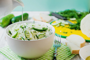  vegetarian Healthy food, light, low calorie fitness salad of fresh cucumbers, cabbage and dill with olive or sunflower oil, spices and salt on a light wooden background 