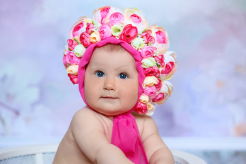 The baby sits in a flower hat. Girl in hat with flowers