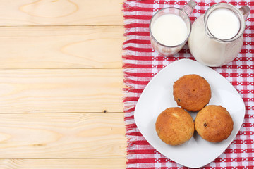 Glass jug pitcher of fresh milk with glass and muffins in a rustic setting on the wooden background  with copy space. Top view.