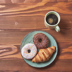 food plate of donut and croissant with mug of coffe on wooden background