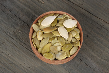 Pumpkin seeds in wooden bowl on wooden background top view with copy space