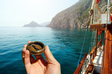 Hand holding old compass on wooden boat in the sea © dimazel