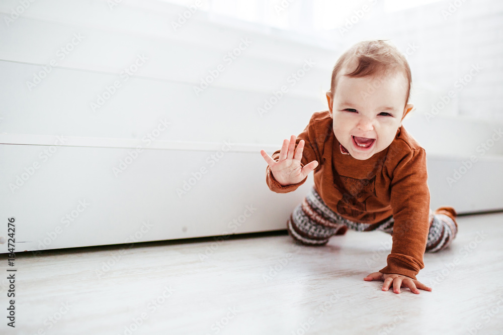 Wall mural happy child in orange sweater plays with feather on the floor